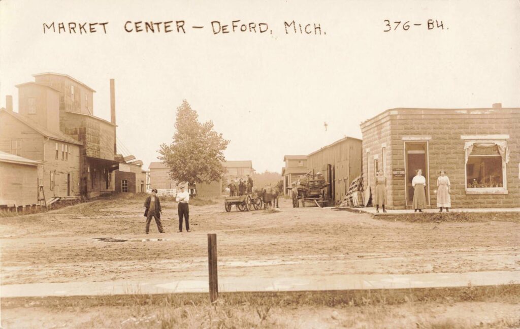 Market Center, Deford, early 1900s. The photo brings together the elevator, nearby stores, and the broad dirt street where buyers, teamsters, and farmers met during harvest trade.