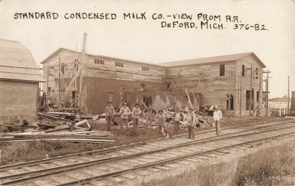 Standard Condensed Milk Company from the railroad side, 1913. The tracks in the foreground show why the site was chosen: the factory depended on rail shipping as much as it depended on milk from local farms. 