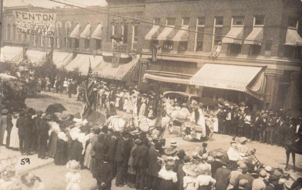 Crowd watching a Fourth of July parade in downtown Fenton Michigan in the early 1900s - small town Michigan 4th of July