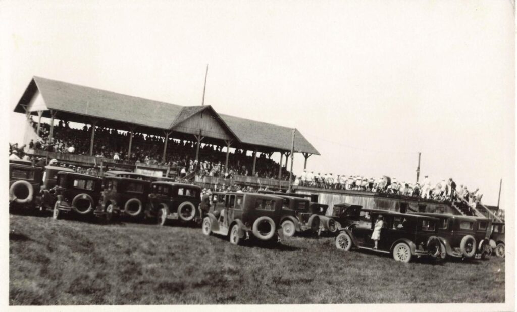 Automobiles parked near a crowded grandstand at a Fourth of July event in North Branch Michigan in 1927