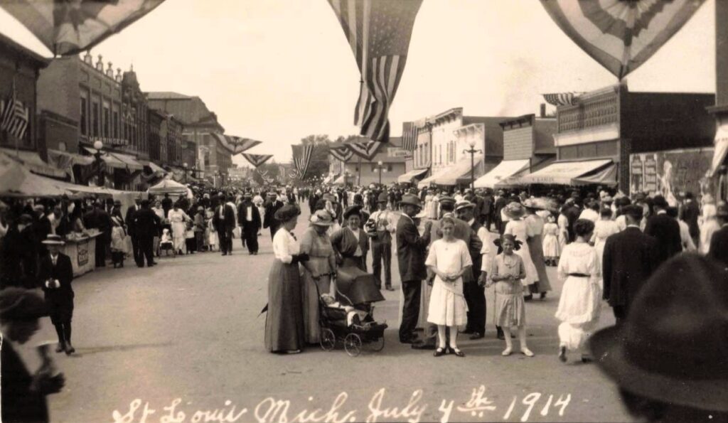 Crowds and large American flags on Main Street during the Fourth of July celebration in St Louis Michigan in 1917