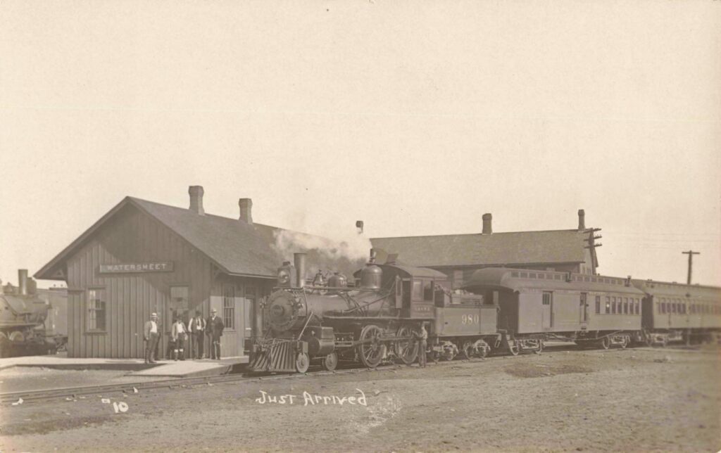 Watersmeet Michigan depot with steam locomotive and passenger cars.