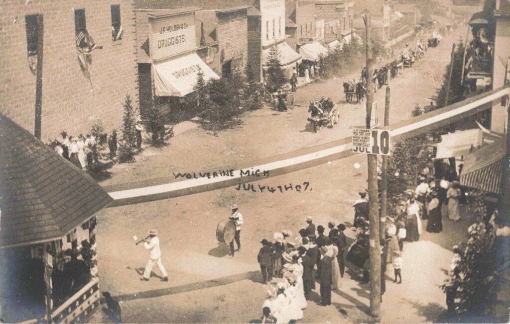 Small Fourth of July parade moving past storefronts in Wolverine Michigan in 1907