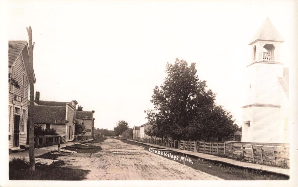 Early 20th-century Cross Village history postcard view with a church tower, boardwalks and an unpaved main road.