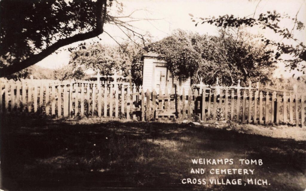 Historic postcard of Father Weikamp’s tomb in Cross Village, Michigan, showing a small fenced crypt and cemetery ground.