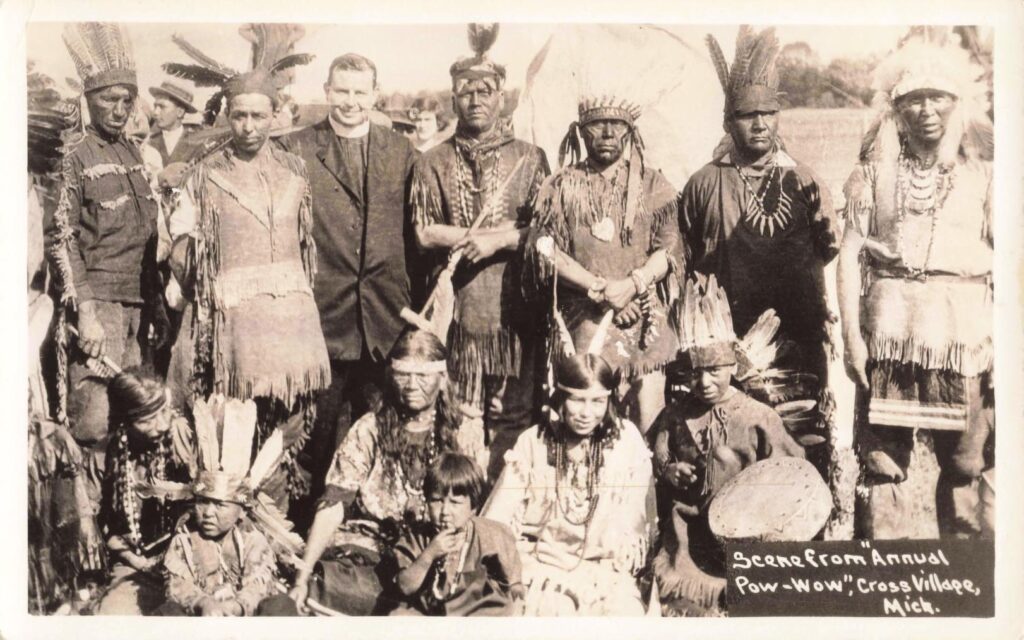 Historic pow-wow group portrait from Cross Village, Michigan, showing Odawa participants, children and a priest.
