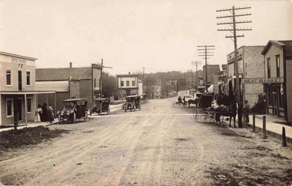Early automobiles and delivery trucks mark Hubbardston’s shift from wagon traffic to the motor age.