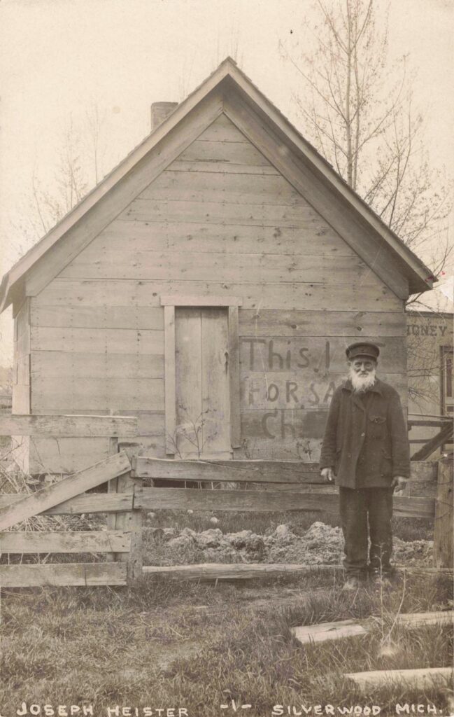 Joseph Heister stands beside a small weathered building. The reason the card was made is not stated.