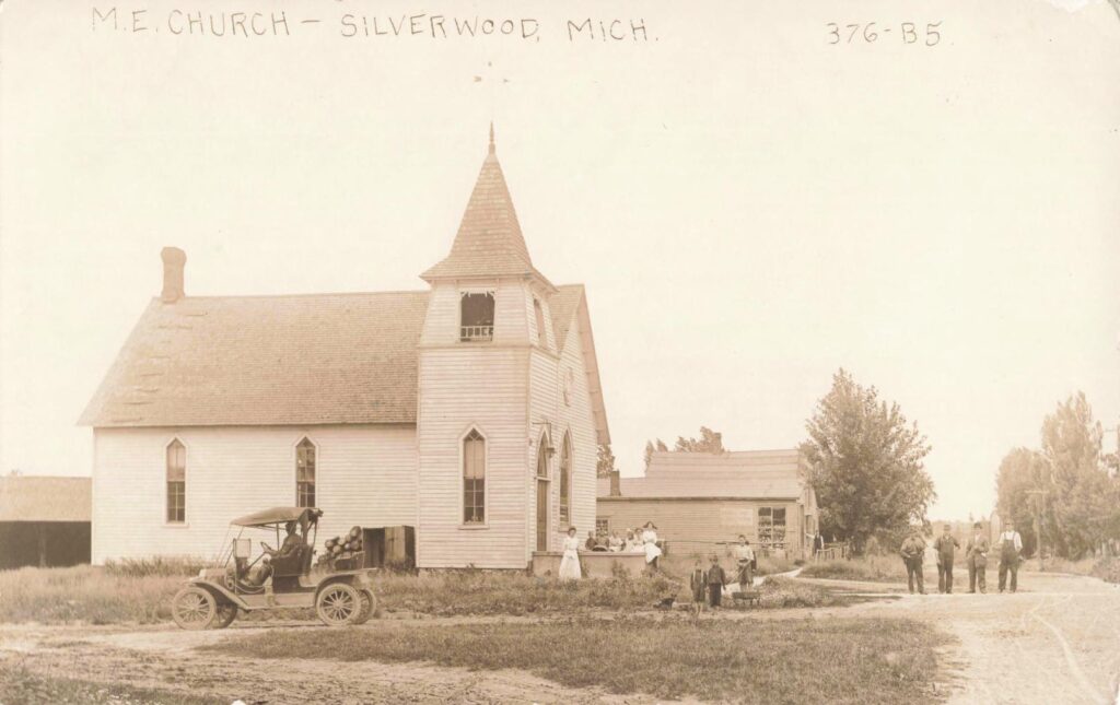Residents gather near Silverwood’s Methodist Episcopal church as an early automobile stands beside the road.