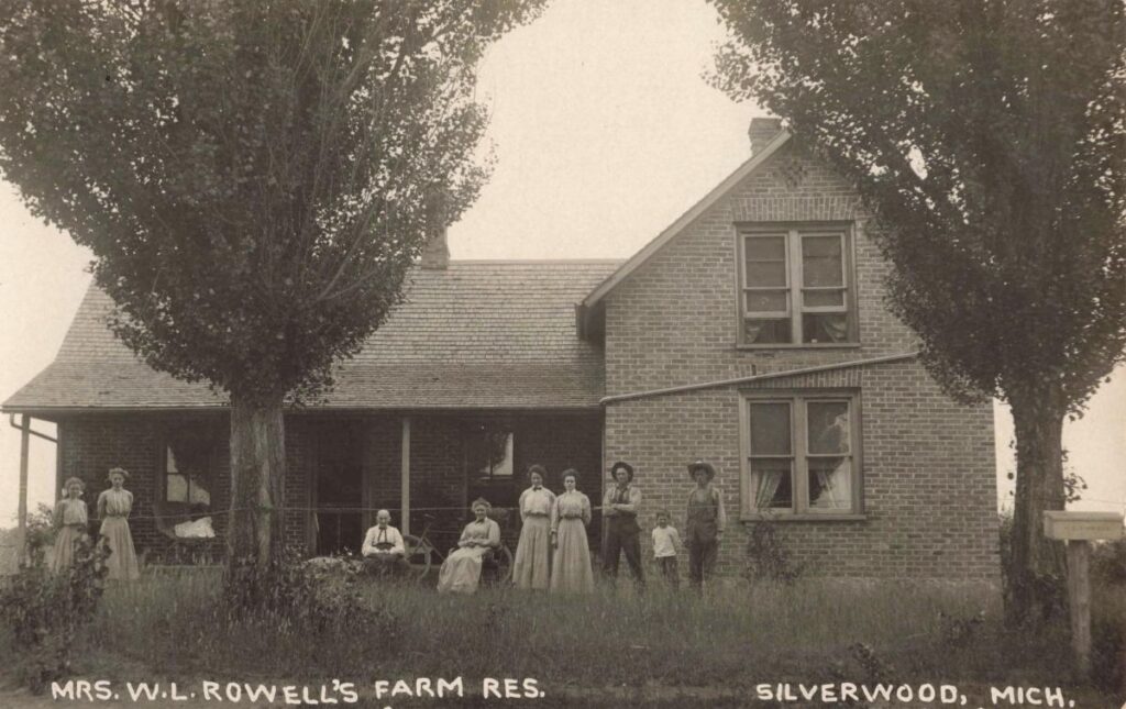 The Rowell residence was a substantial brick farmhouse. The card’s Silverwood label and the Lapeer County plat show how the community extended across the county line.