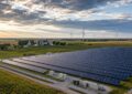 Rows of solar panels on Michigan farmland with wind turbines visible in the distance