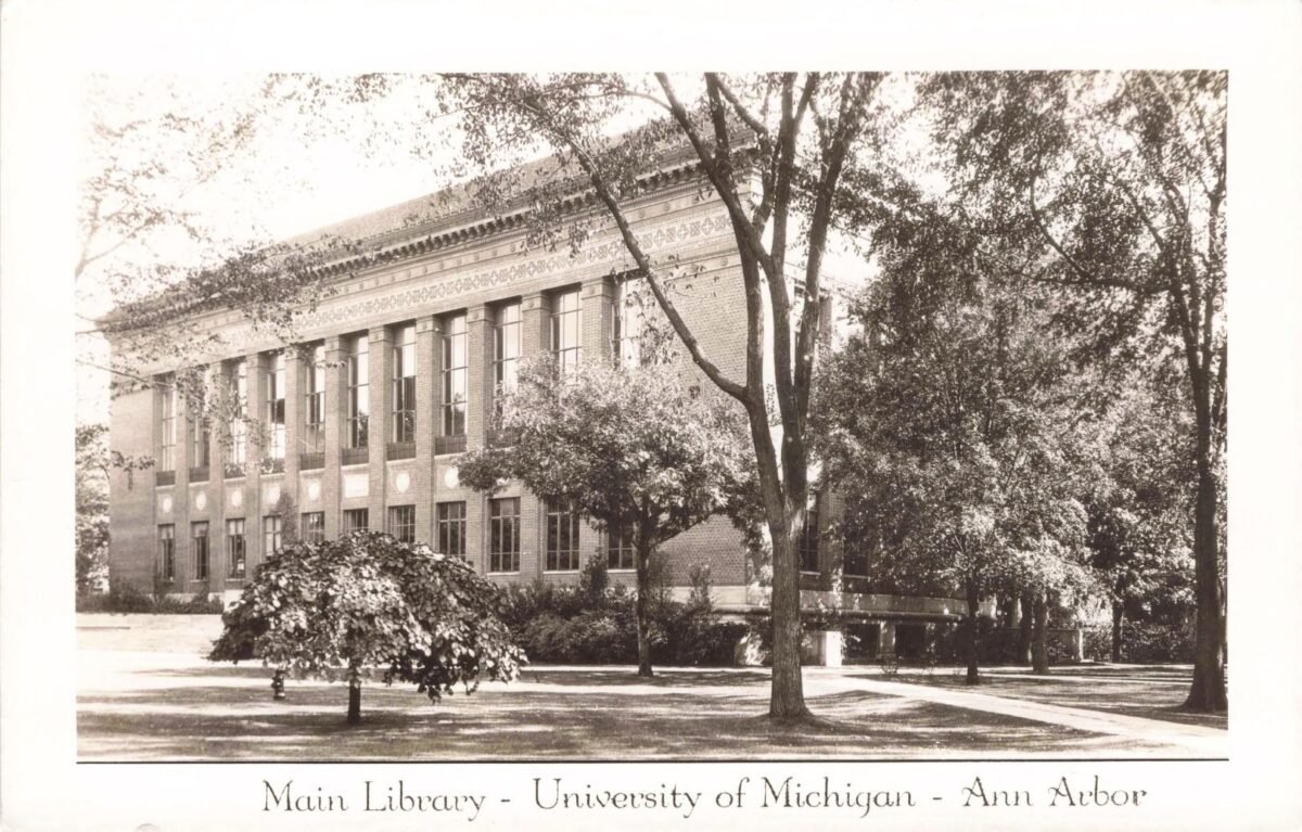 Historic view of the University of Michigan’s brick Main Library in Ann Arbor, surrounded by trees and lawn.