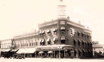 Black-and-white view of the three-story brick Clintonian Hotel in downtown Clinton, Michigan, with striped window awnings, parked automobiles, storefronts and a suspended traffic signal.