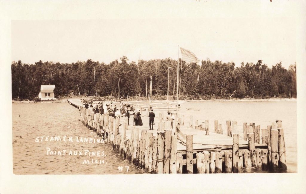 Historic postcard showing people on the wooden steamer landing at Pointe Aux Pins, Michigan, with sailboats and an American flag.