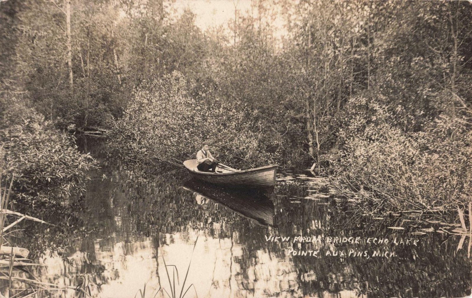 Historic Pointe Aux Pins postcard showing a man in a wooden boat near a small bridge on Echo Lake on Bois Blanc Island.