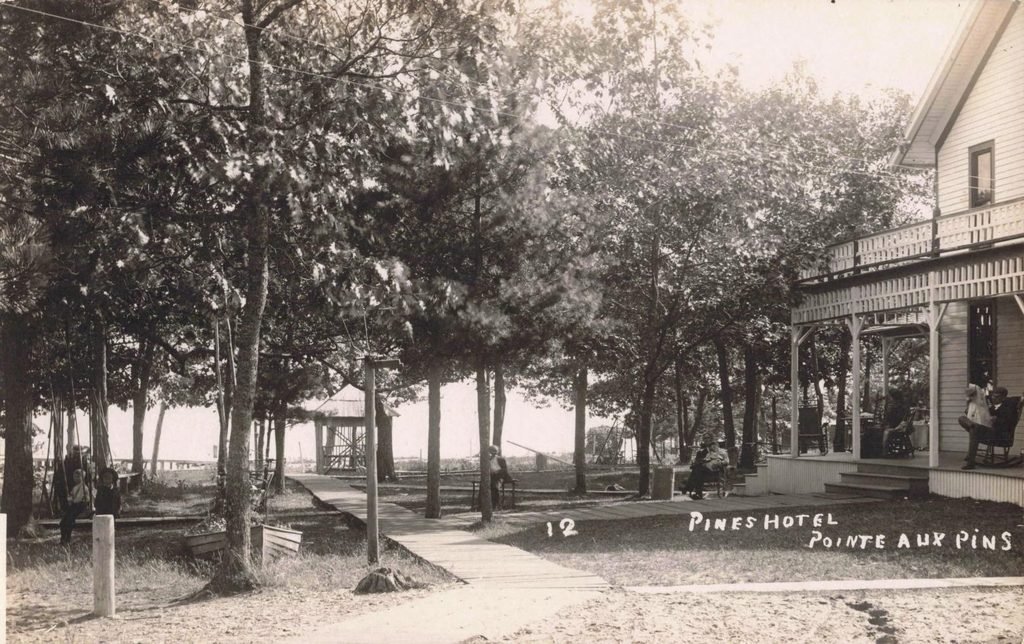 Historic postcard of the Pines Hotel at Pointe Aux Pins, Michigan, showing large porches, trees and a wooden walkway near Lake Huron.