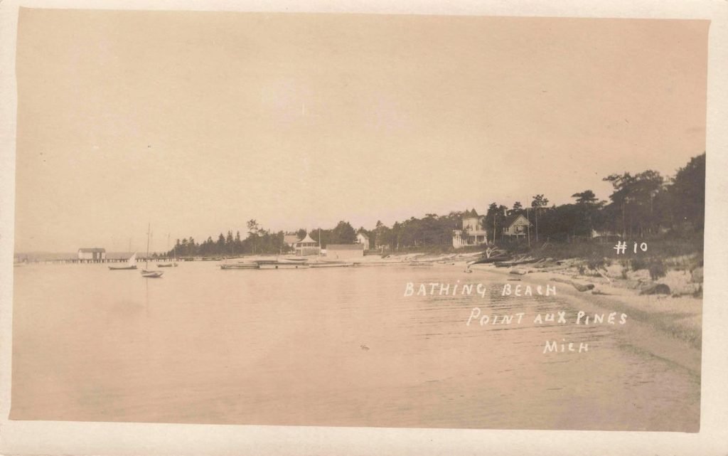 Historic postcard showing the Lake Huron bathing beach at Pointe Aux Pins, Michigan, with shoreline and docks in the distance.