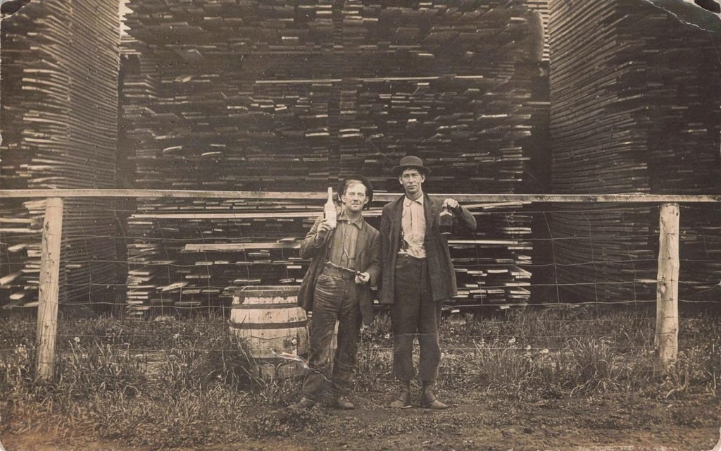 Two men standing in front of large stacks of cut lumber in Clifford Michigan.