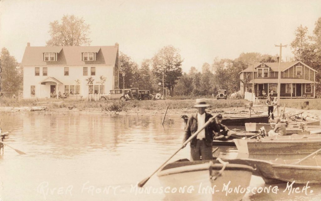 Small wooden boats and people at the landing in front of the inn and a porch-fronted neighboring building. The man holding the oar has not been identified; the view is undated. Source: University of Michigan, item 11603.