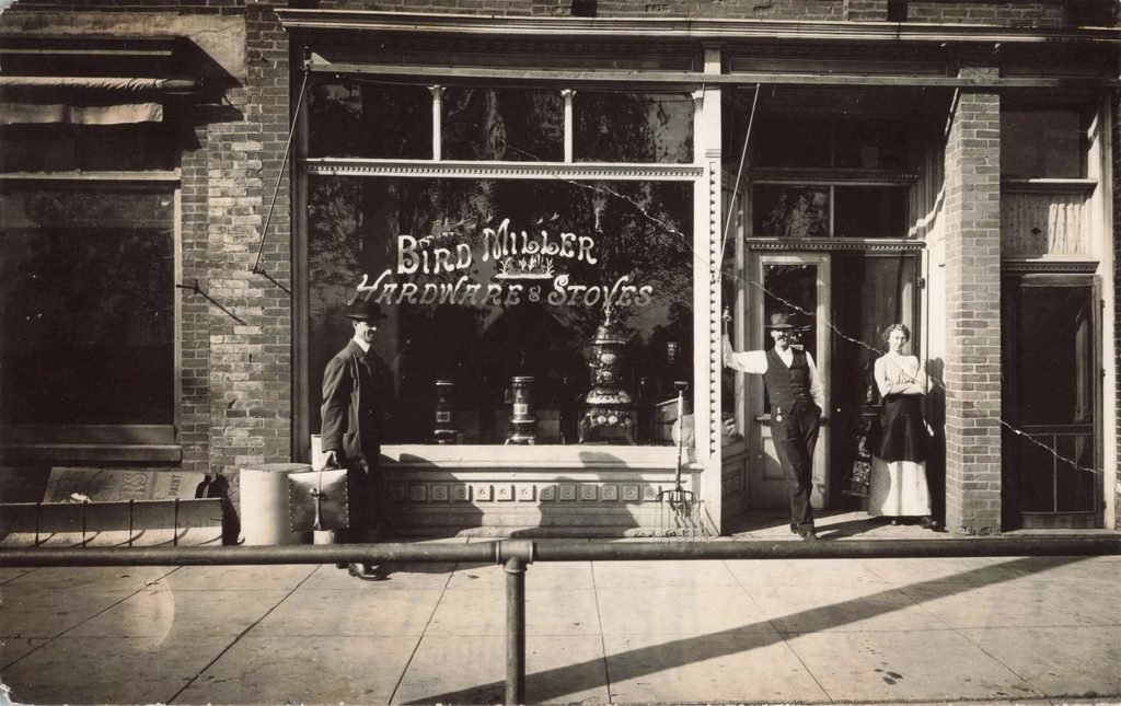 Bird Miller Hardware and Stoves storefront in Clifford Michigan with three people standing outside and stoves visible in the window.