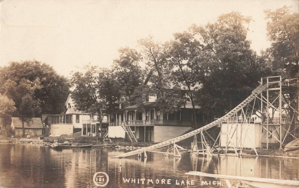 Long wooden slide descending from an elevated tower into the lake near shorefront buildings