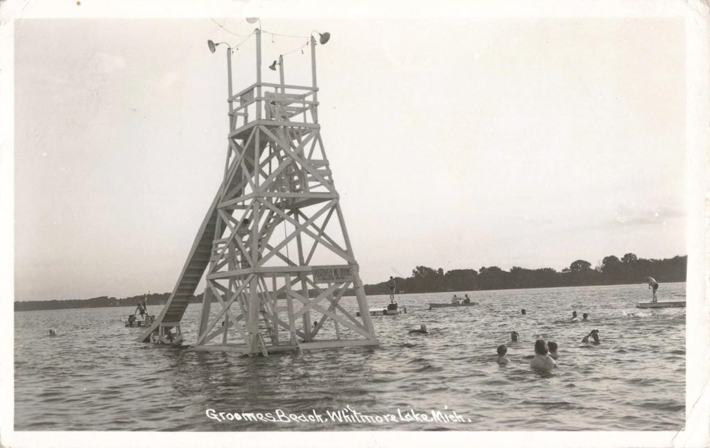Tall wooden diving and slide structure set in Whitmore Lake, surrounded by swimmers
