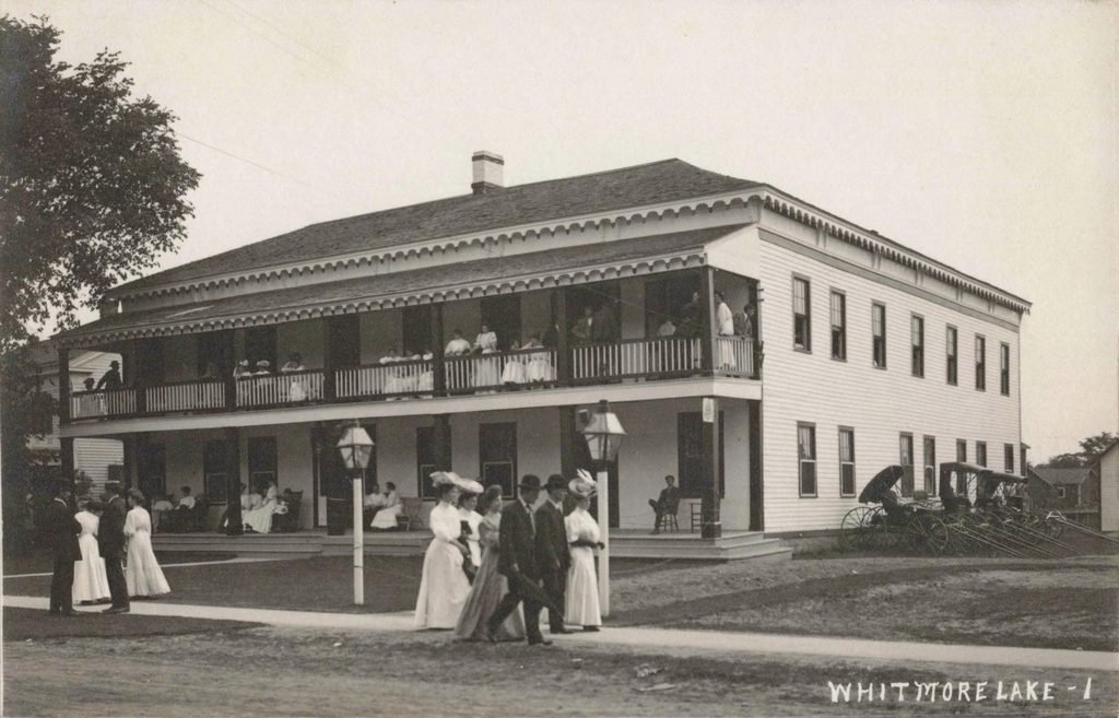 Two-story lakeside hotel with a long veranda, trees and a lawn beside a path
