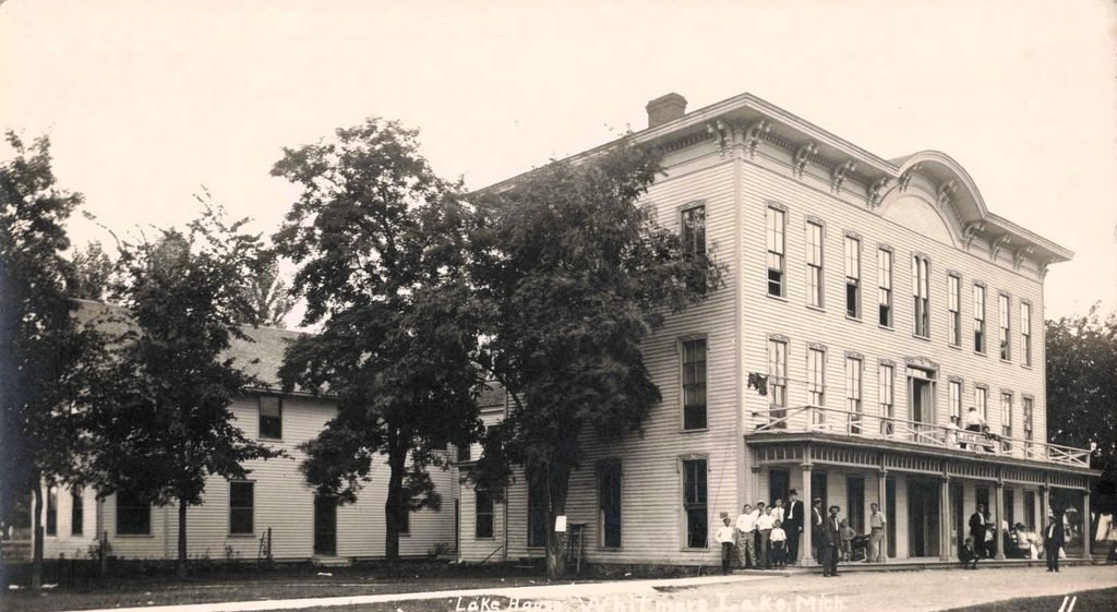 Substantial three-story brick building with storefronts and street trees in early Whitmore Lake