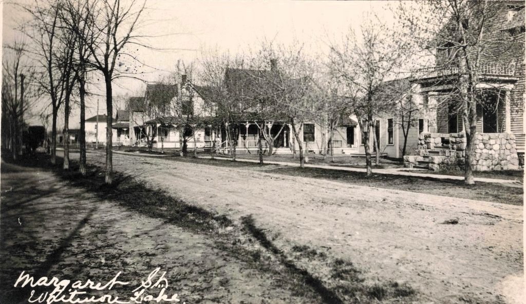 Unpaved tree-lined street with sidewalk and houses in Whitmore Lake, annotated by the postcard sender